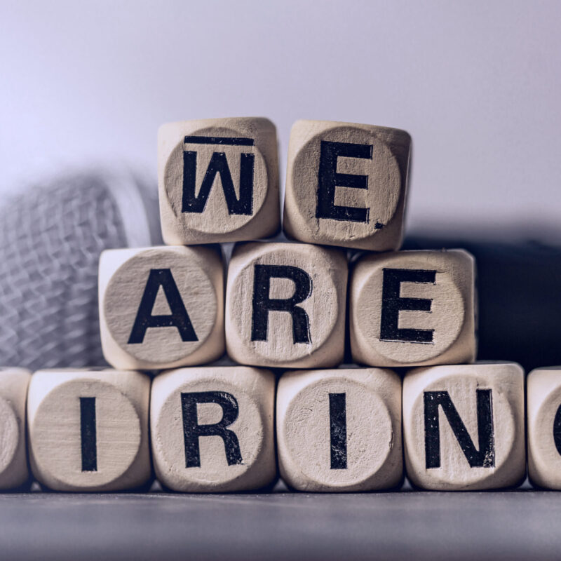 Block wood text with we are hiring and blurred microphone backgr